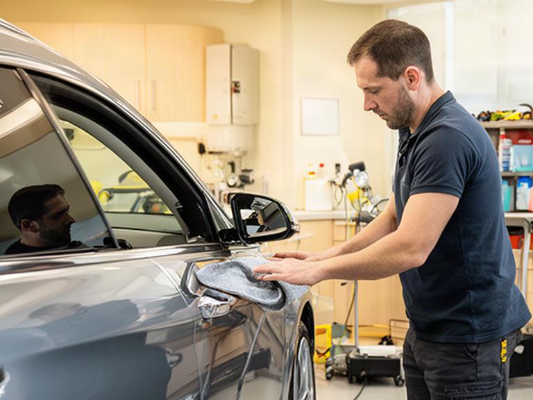 明るいスクール施設で自動車の側面を確認するディテイリング講師