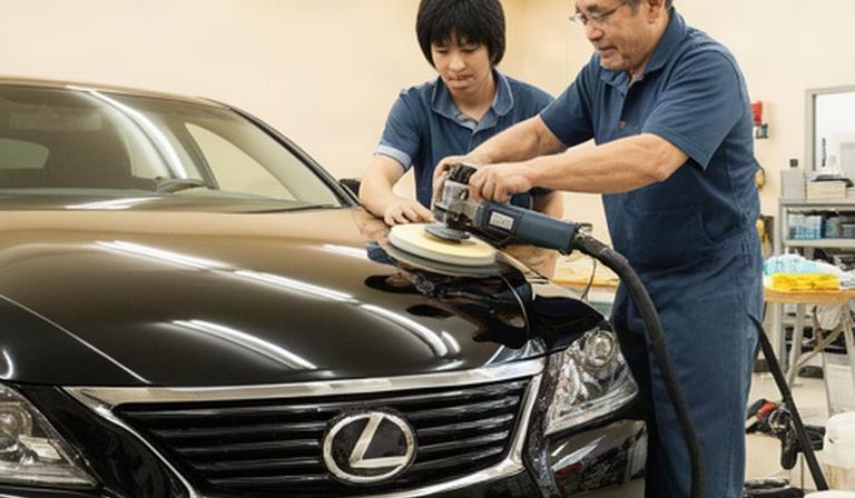 明るい施工スペースで黒い自動車を磨く受講生と講師