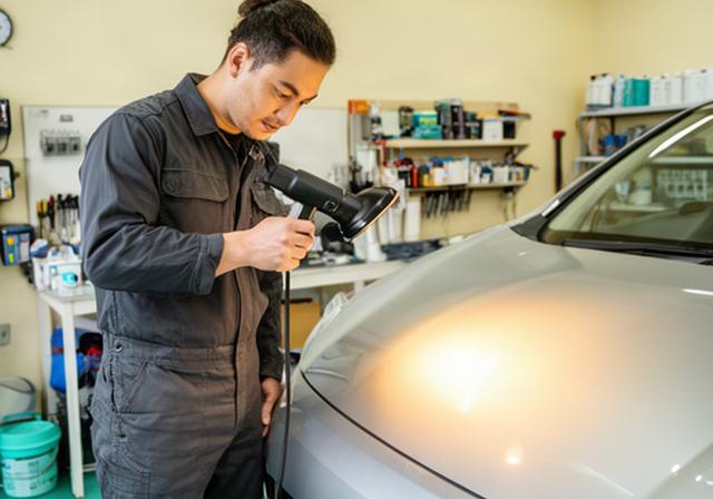 千葉の明るい実習ガレージで車体の塗装面をライトで確認する講師